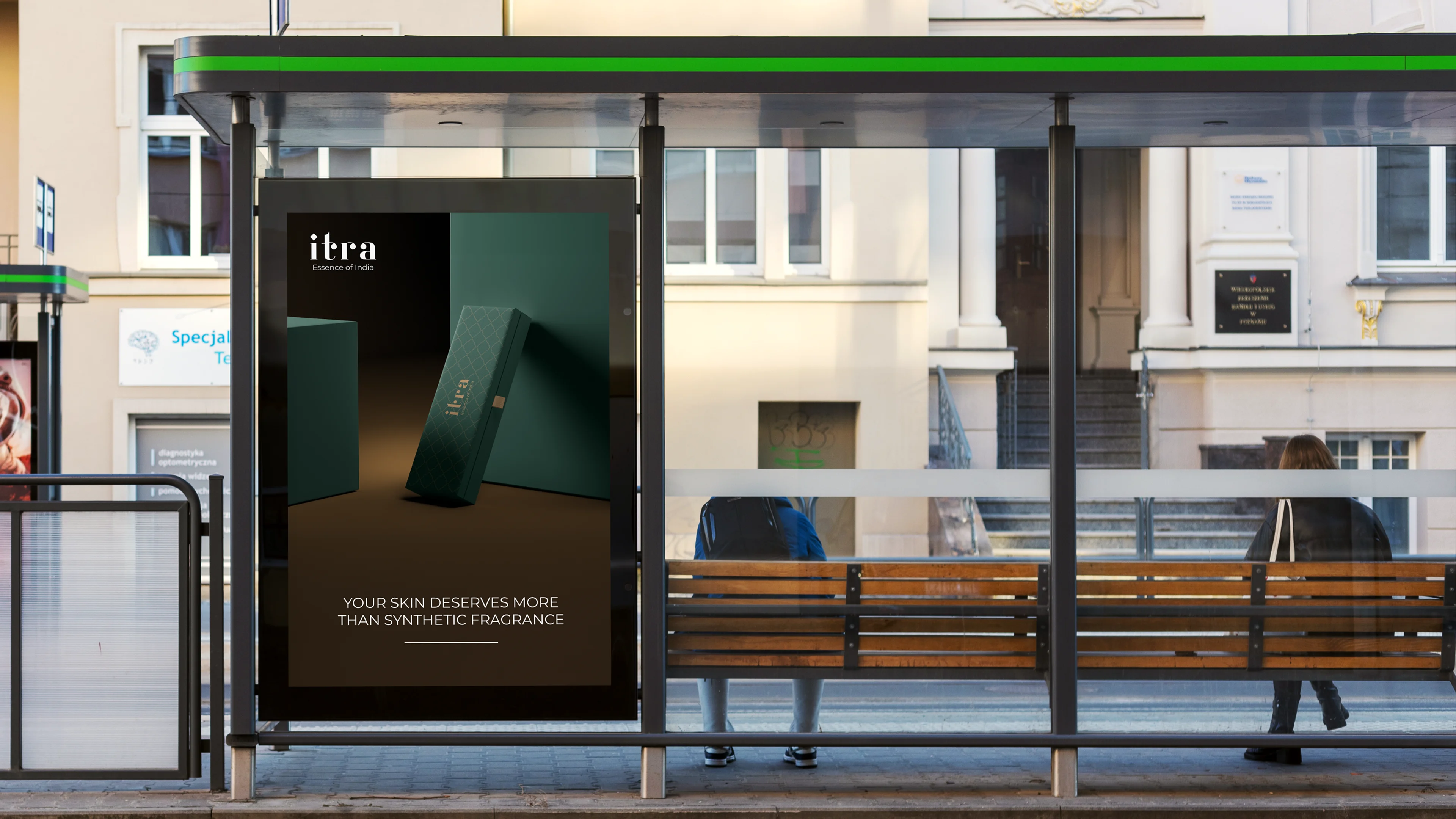 Itra OOH poster on a backlit bus shelter display, showing a dramatically lit product box against a dark background with the line: Your skin deserves more than synthetic fragrance