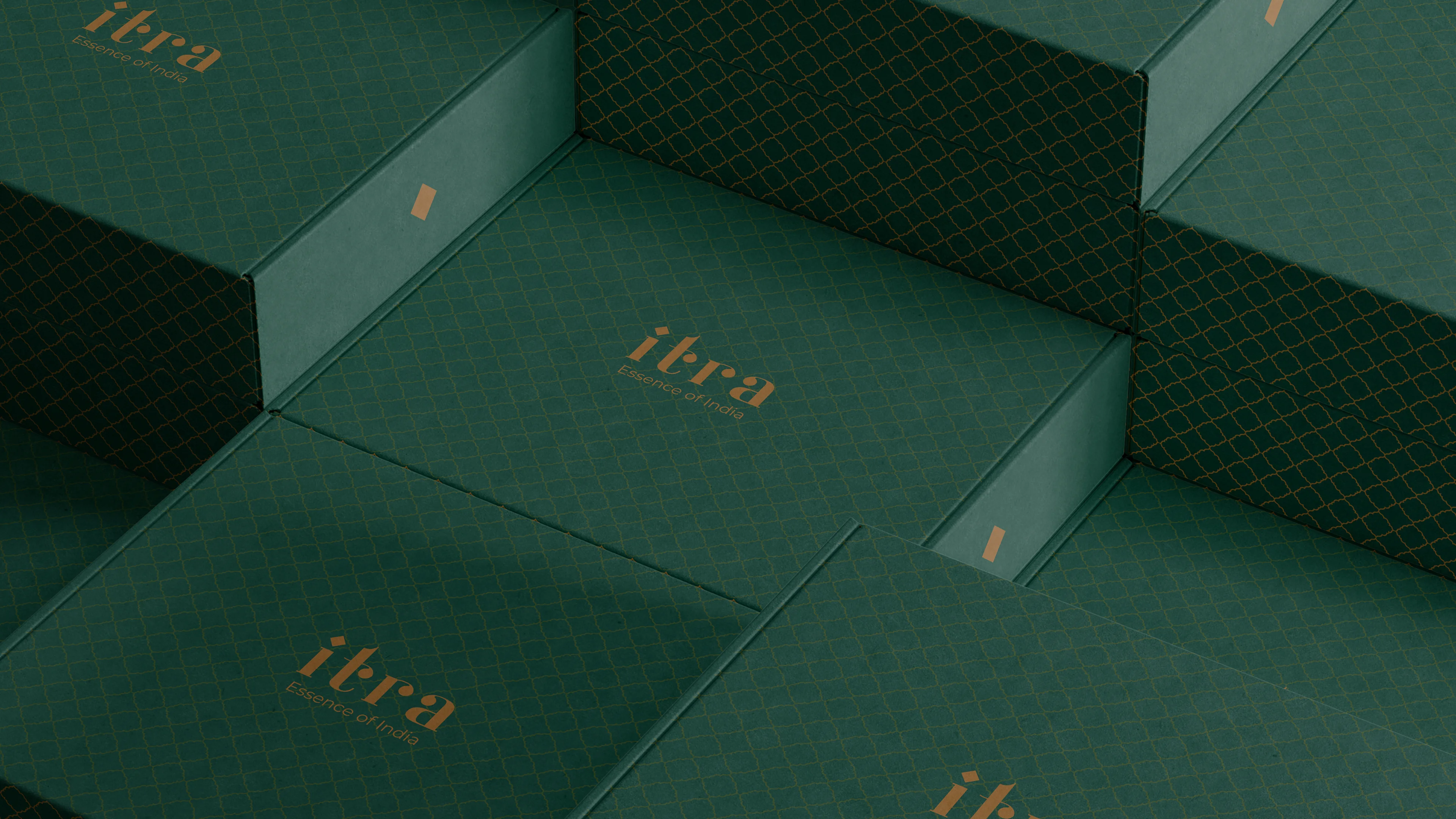 Stacked Itra mailer boxes in forest green with full-coverage gold lattice pattern and wordmark, seen from a top-down angle showing the pattern repeating at volume